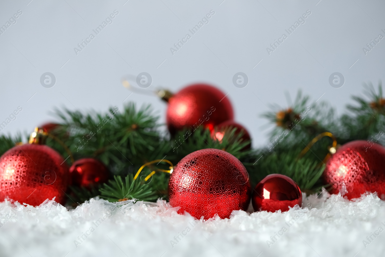 Beautiful Christmas balls and fir branches on snow against grey background. Space for text Photo of Beautiful Christmas balls and fir branches on snow against grey background. Space for text