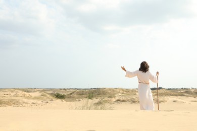 Jesus Christ raising hand in desert, back view. Space for text Photo of Jesus Christ raising hand in desert, back view. Space for text