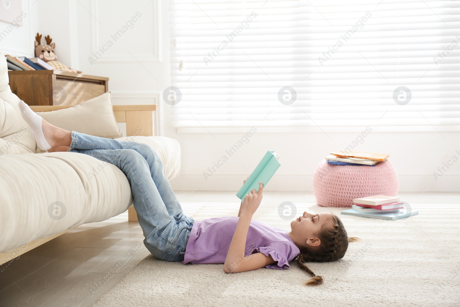 Cute little girl reading book on floor at home Photo of Cute little girl reading book on floor at home