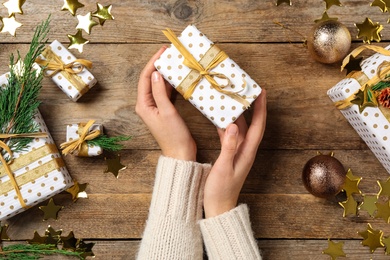 Woman holding Christmas gift box with golden bow at wooden table, top view Photo of Woman holding Christmas gift box with golden bow at wooden table, top view