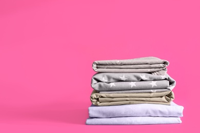 Stack of clean bed sheets on pink background. Space for text Photo of Stack of clean bed sheets on pink background. Space for text