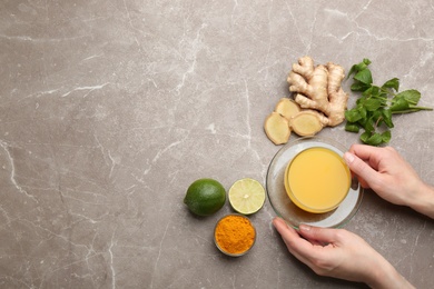 Woman holding cup of immunity boosting drink at table with ingredients, top view. Space for text Photo of Woman holding cup of immunity boosting drink at table with ingredients, top view. Space for text