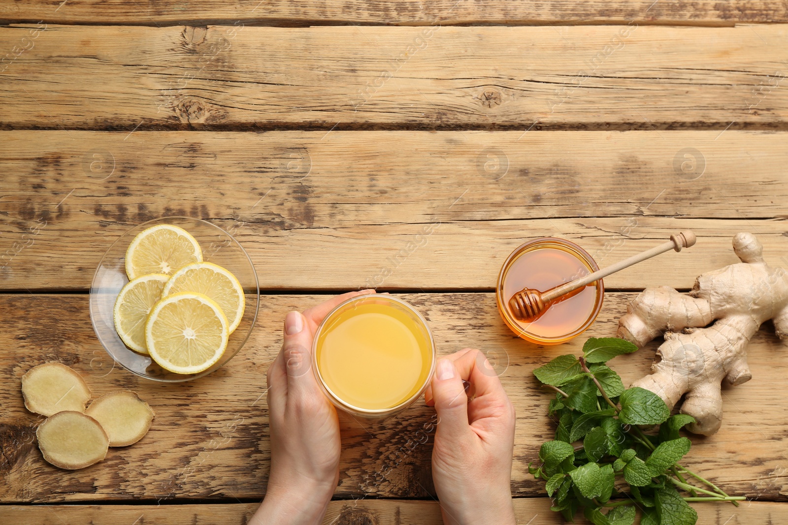 Woman holding cup of immunity boosting drink at wooden table with ingredients, top view. Space for text Photo of Woman holding cup of immunity boosting drink at wooden table with ingredients, top view. Space for text
