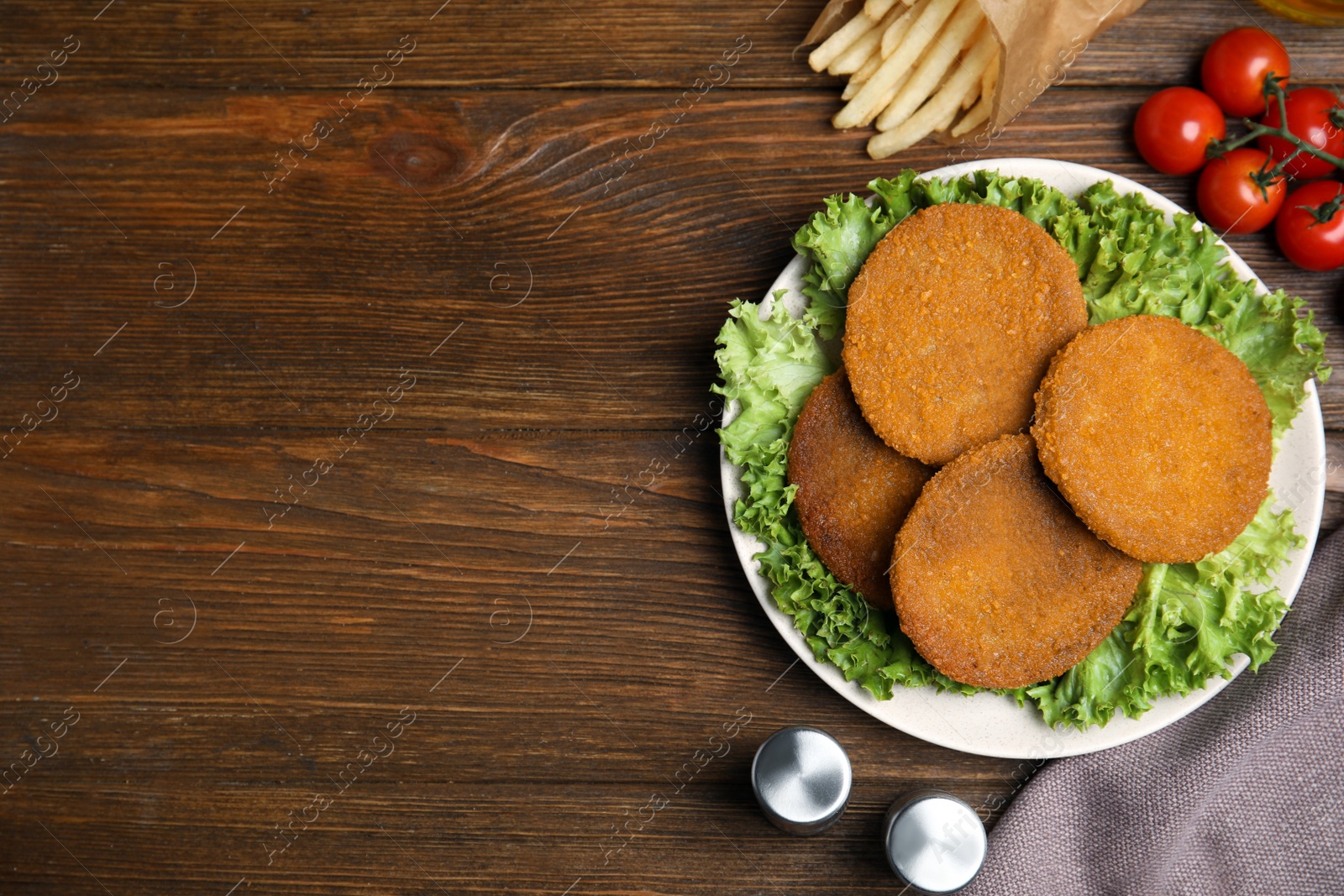 Delicious fried breaded cutlets, spices and cherry tomatoes on wooden table, flat lay. Space for text Photo of Delicious fried breaded cutlets, spices and cherry tomatoes on wooden table, flat lay. Space for text