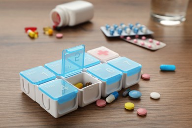 Plastic box with different pills on wooden table Photo of Plastic box with different pills on wooden table