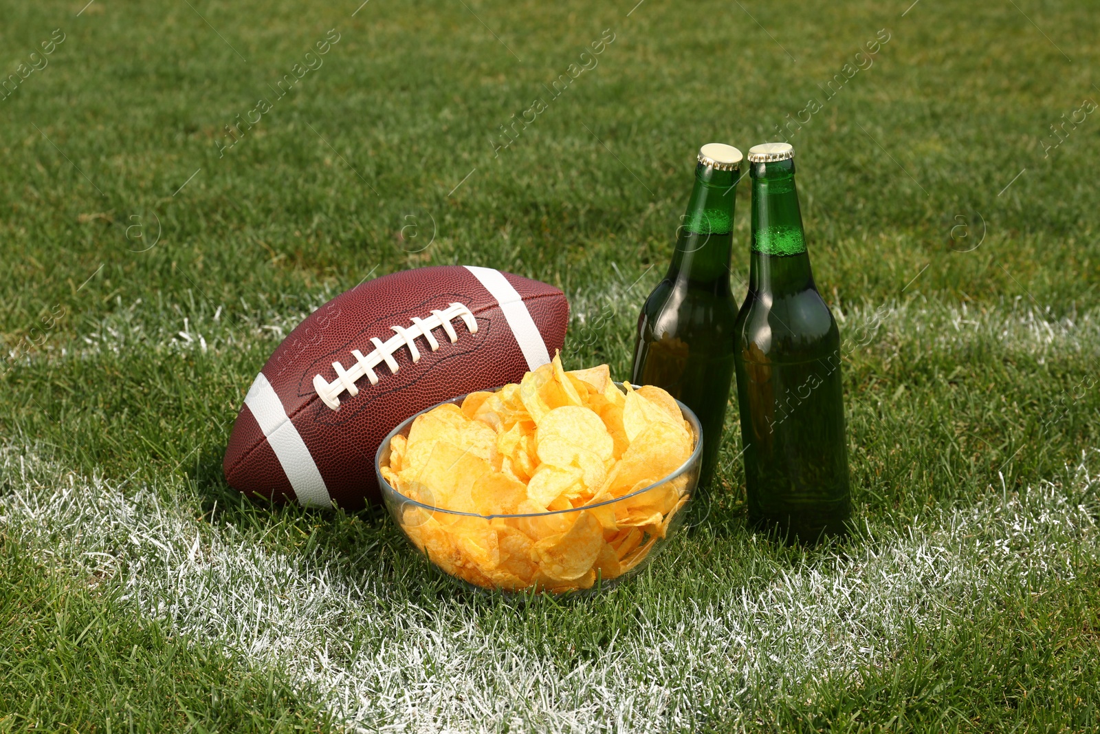 American football ball with beer and chips on green field grass outdoors Photo of American football ball with beer and chips on green field grass outdoors