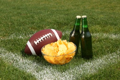 American football ball with beer and chips on green field grass outdoors Photo of American football ball with beer and chips on green field grass outdoors