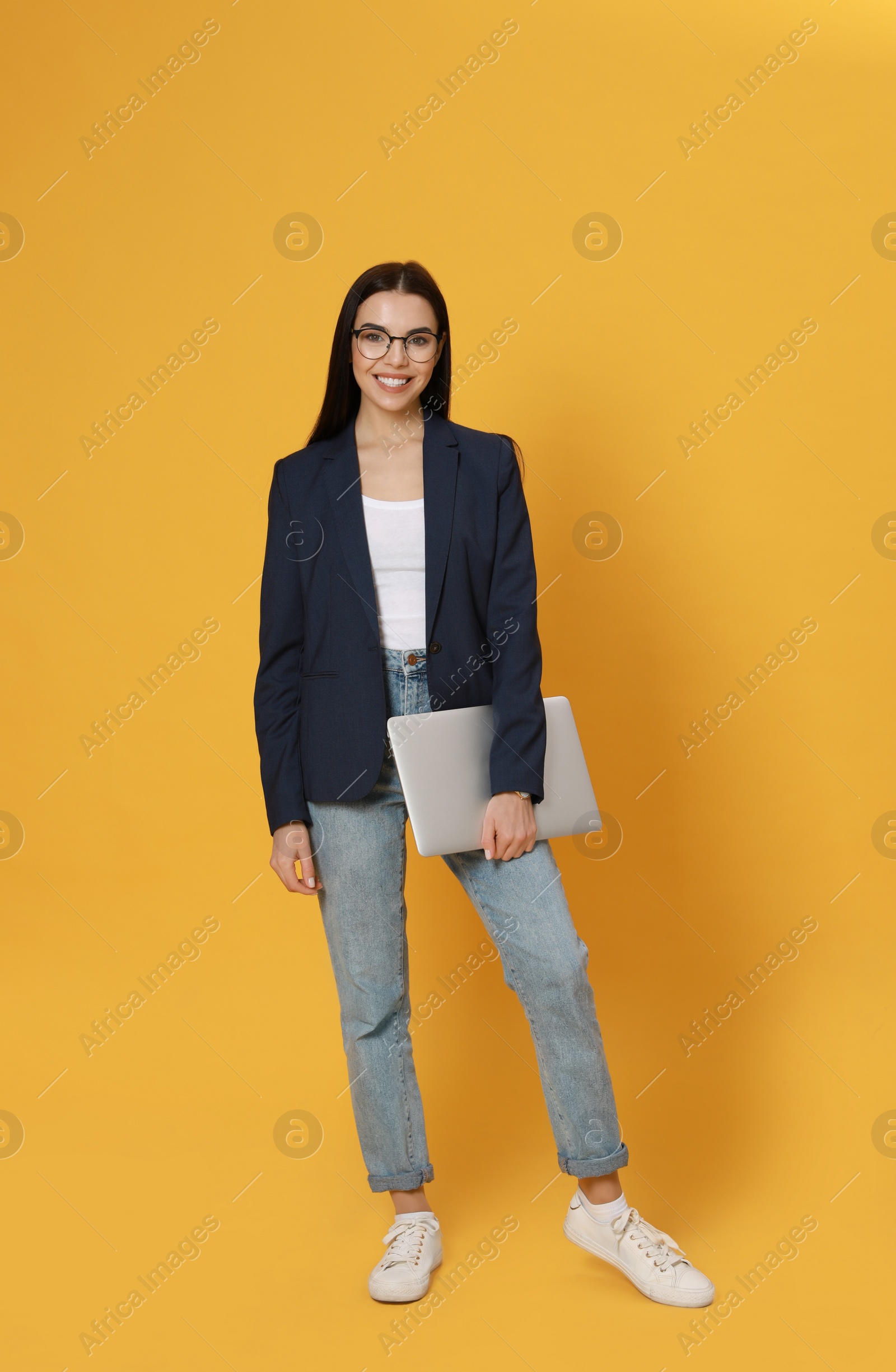 Young woman with modern laptop on yellow background Photo of Young woman with modern laptop on yellow background