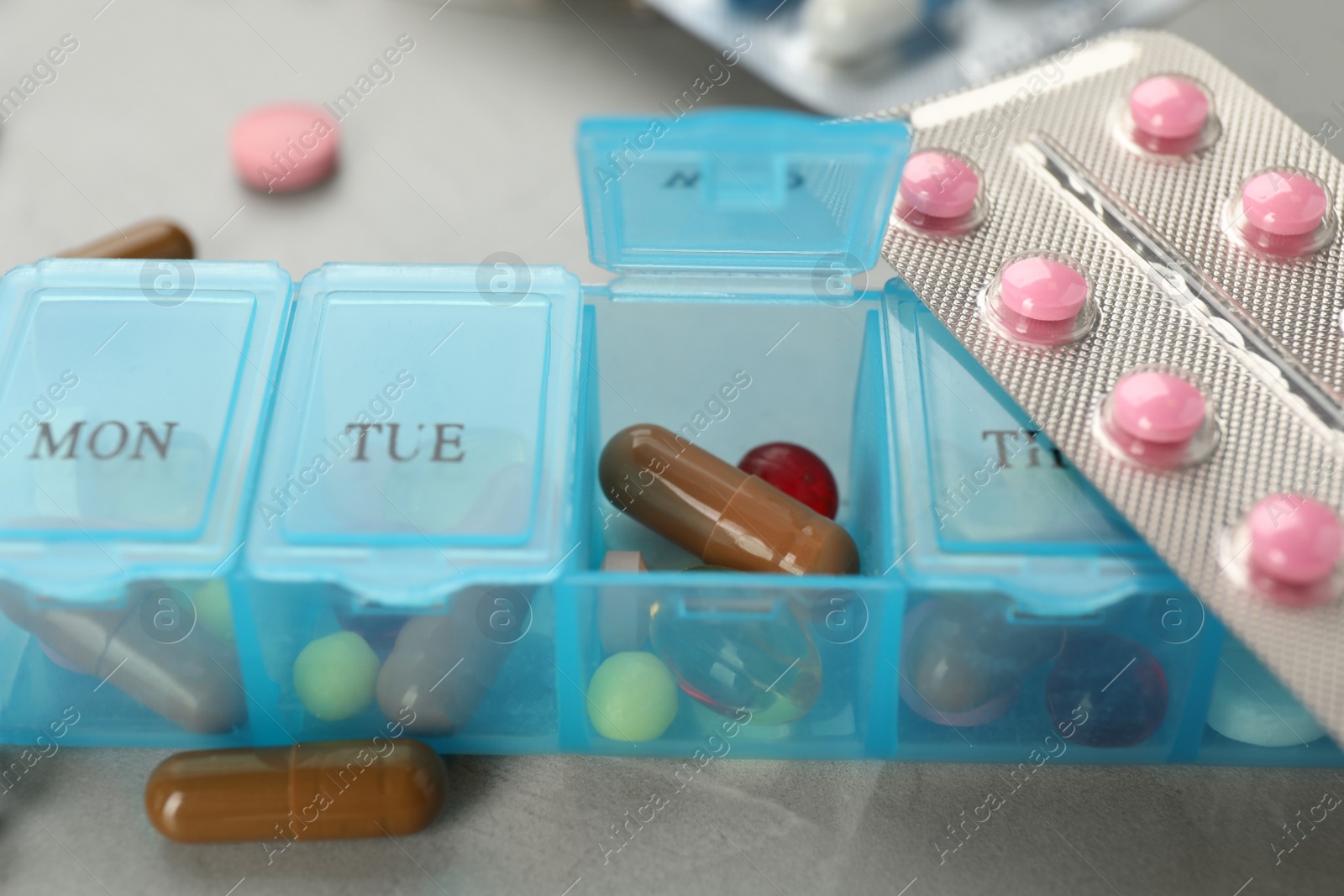 Photo of Plastic box with different pills on light grey stone table, closeup