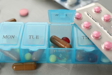 Plastic box with different pills on light grey stone table, closeup Photo of Plastic box with different pills on light grey stone table, closeup