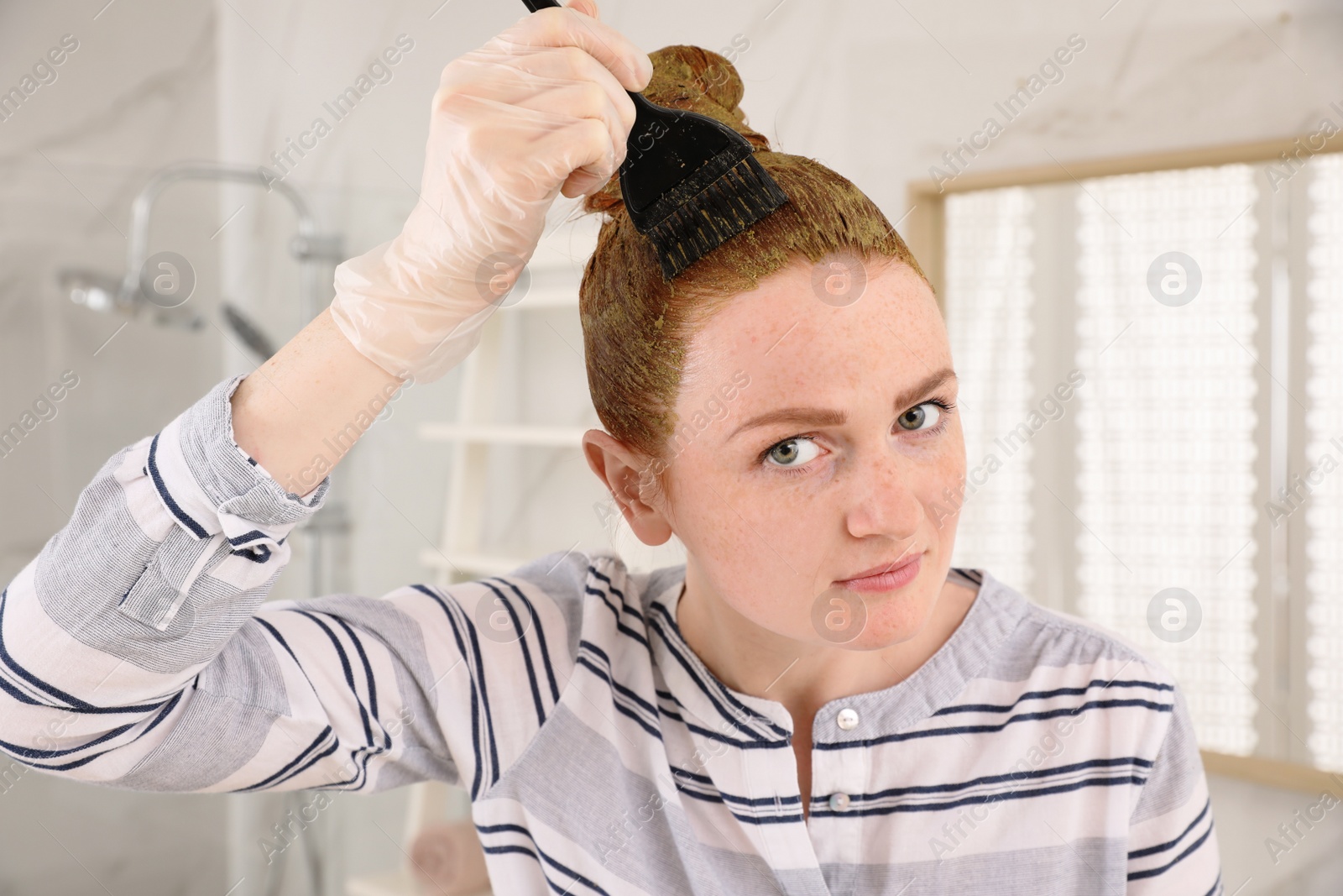 Young woman dyeing her hair with henna in bathroom Photo of Young woman dyeing her hair with henna in bathroom
