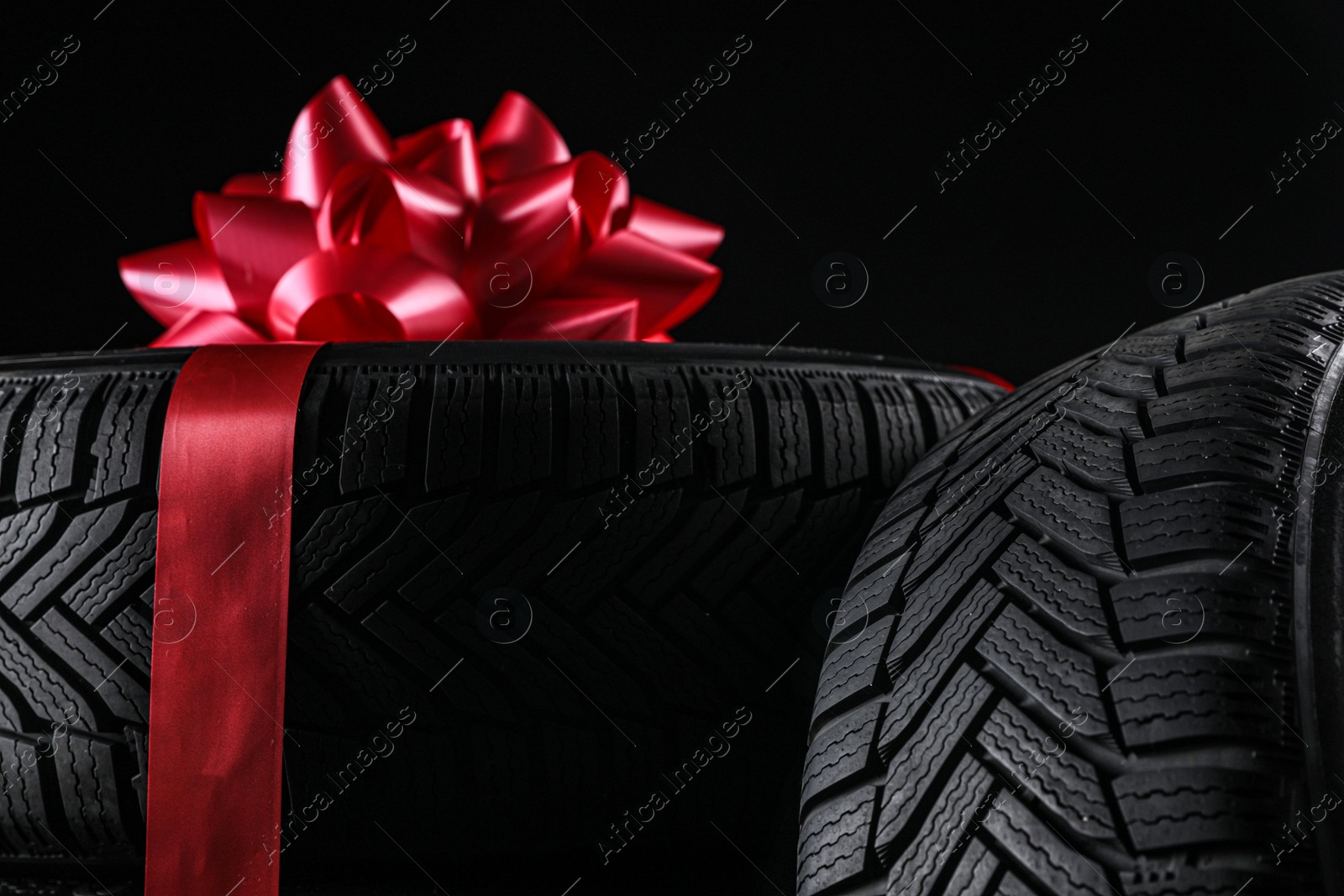 Winter tires with red ribbon on black background, closeup Photo of Winter tires with red ribbon on black background, closeup
