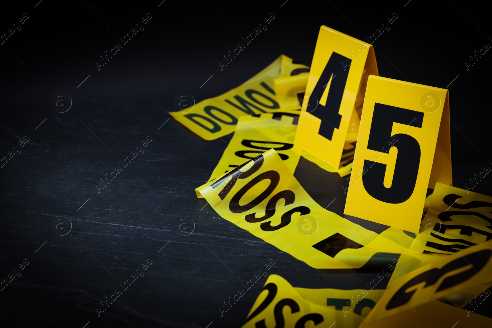 Crime scene tape and evidence markers on black slate background, closeup. Space for text Photo of Crime scene tape and evidence markers on black slate background, closeup. Space for text