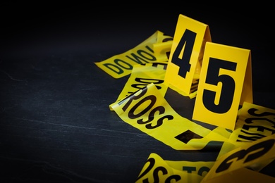 Photo of Crime scene tape and evidence markers on black slate background, closeup. Space for text
