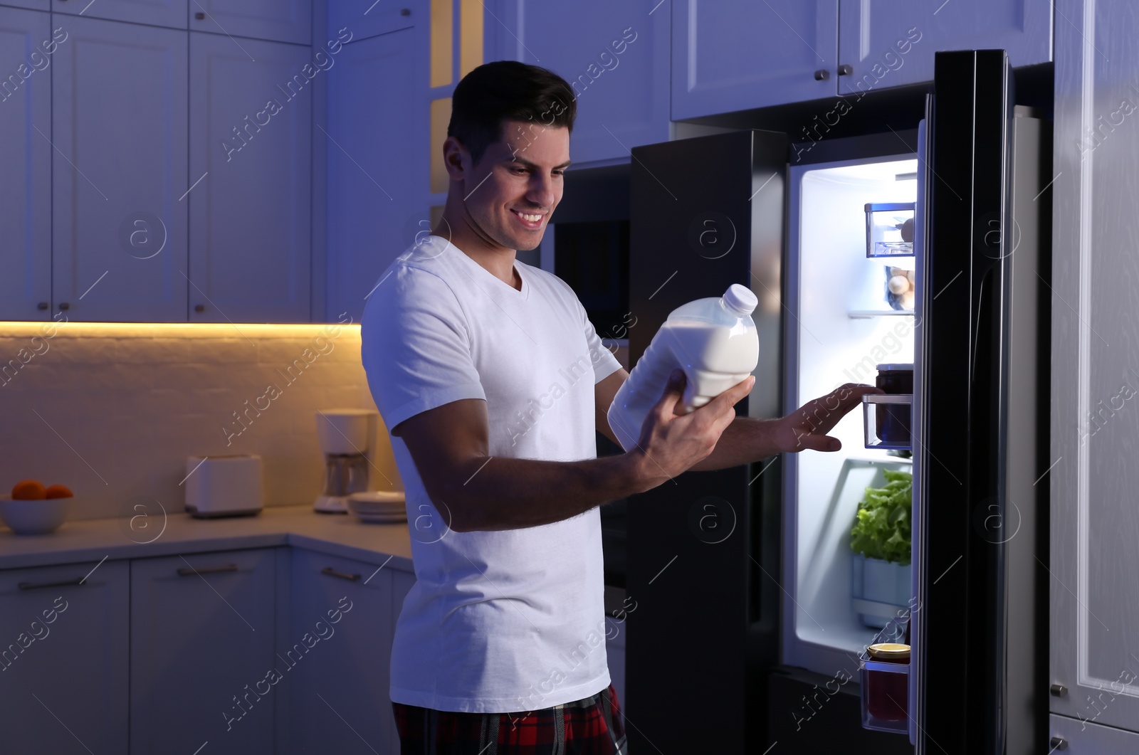 Photo of Man holding gallon bottle of milk near refrigerator in kitchen at night