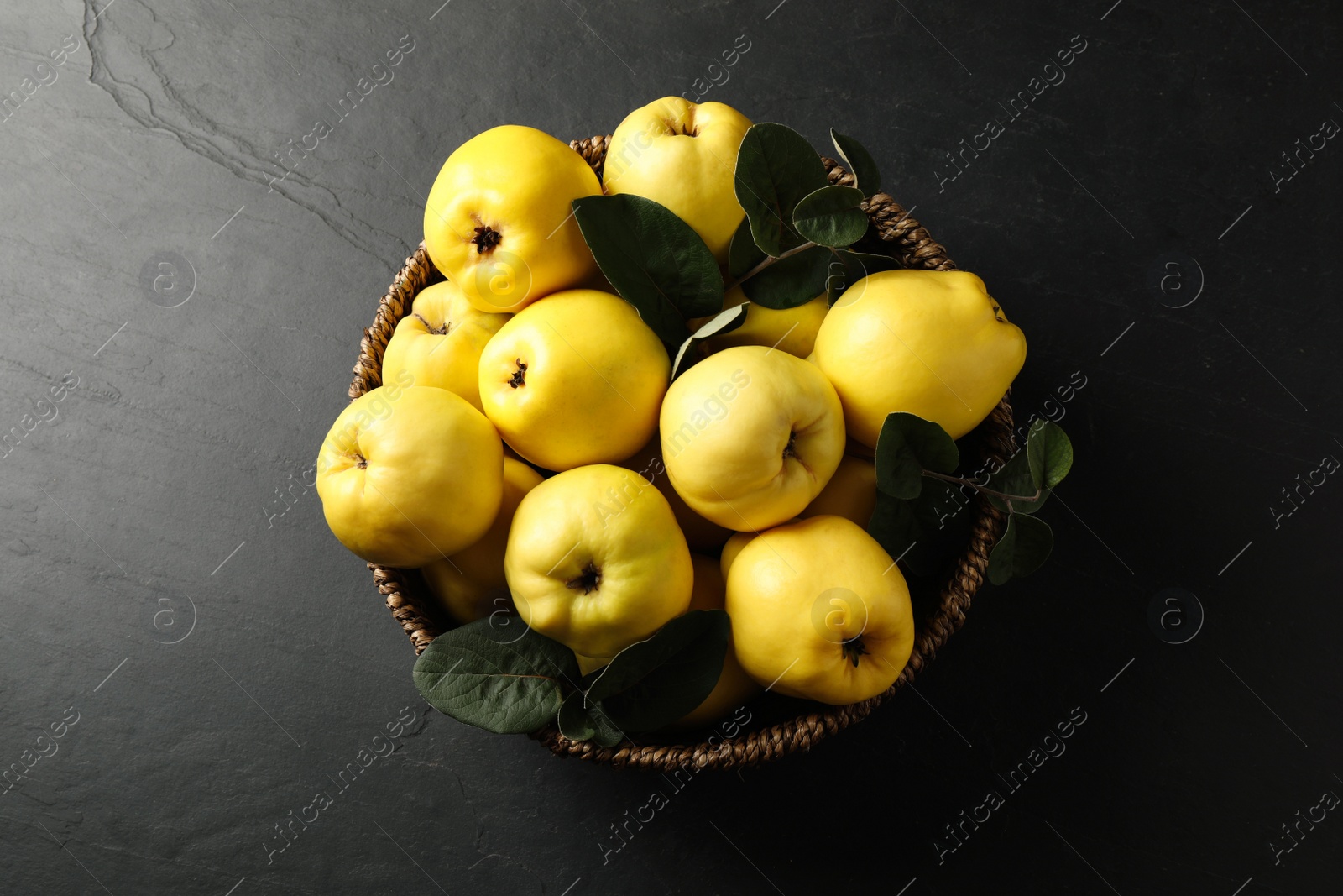 Fresh ripe organic quinces with leaves in wicker basket on black table, top view Photo of Fresh ripe organic quinces with leaves in wicker basket on black table, top view