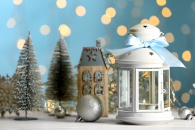 Photo of Christmas lantern with burning candle and festive decor on white table against blurred lights