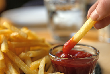 Woman dipping French fries into red sauce in cafe, closeup Photo of Woman dipping French fries into red sauce in cafe, closeup