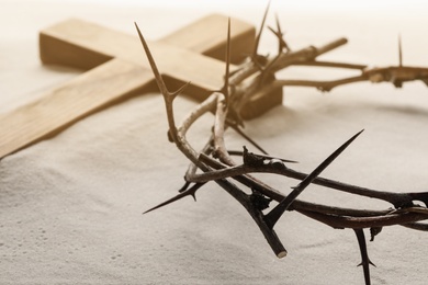 Crown of thorns and wooden cross on sand, closeup. Easter attributes Photo of Crown of thorns and wooden cross on sand, closeup. Easter attributes