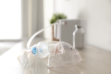 Face mask near modern nebulizer on wooden table indoors. Inhalation equipment Photo of Face mask near modern nebulizer on wooden table indoors. Inhalation equipment