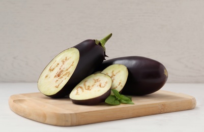 Cut and whole purple eggplants with basil on white table Photo of Cut and whole purple eggplants with basil on white table