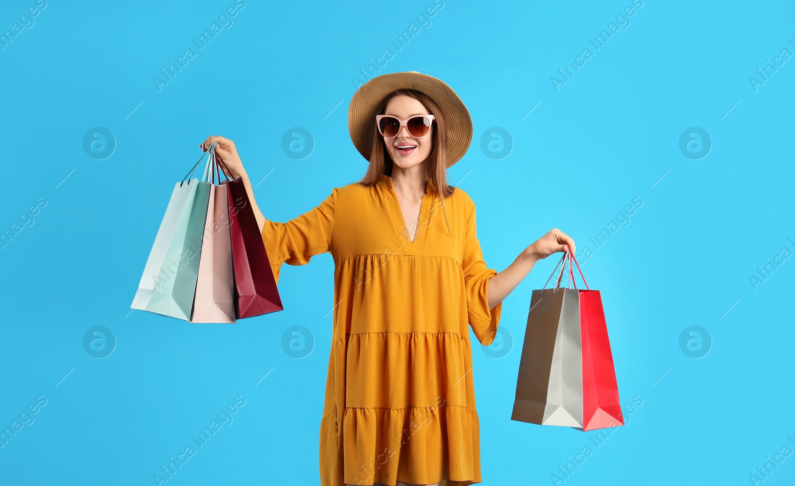 Beautiful young woman with paper shopping bags on light blue background Photo of Beautiful young woman with paper shopping bags on light blue background