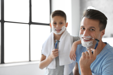 Happy father and son with shaving foam on their faces in bathroom Photo of Happy father and son with shaving foam on their faces in bathroom