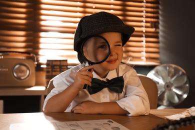 Cute little detective with magnifying glass at table in office Photo of Cute little detective with magnifying glass at table in office