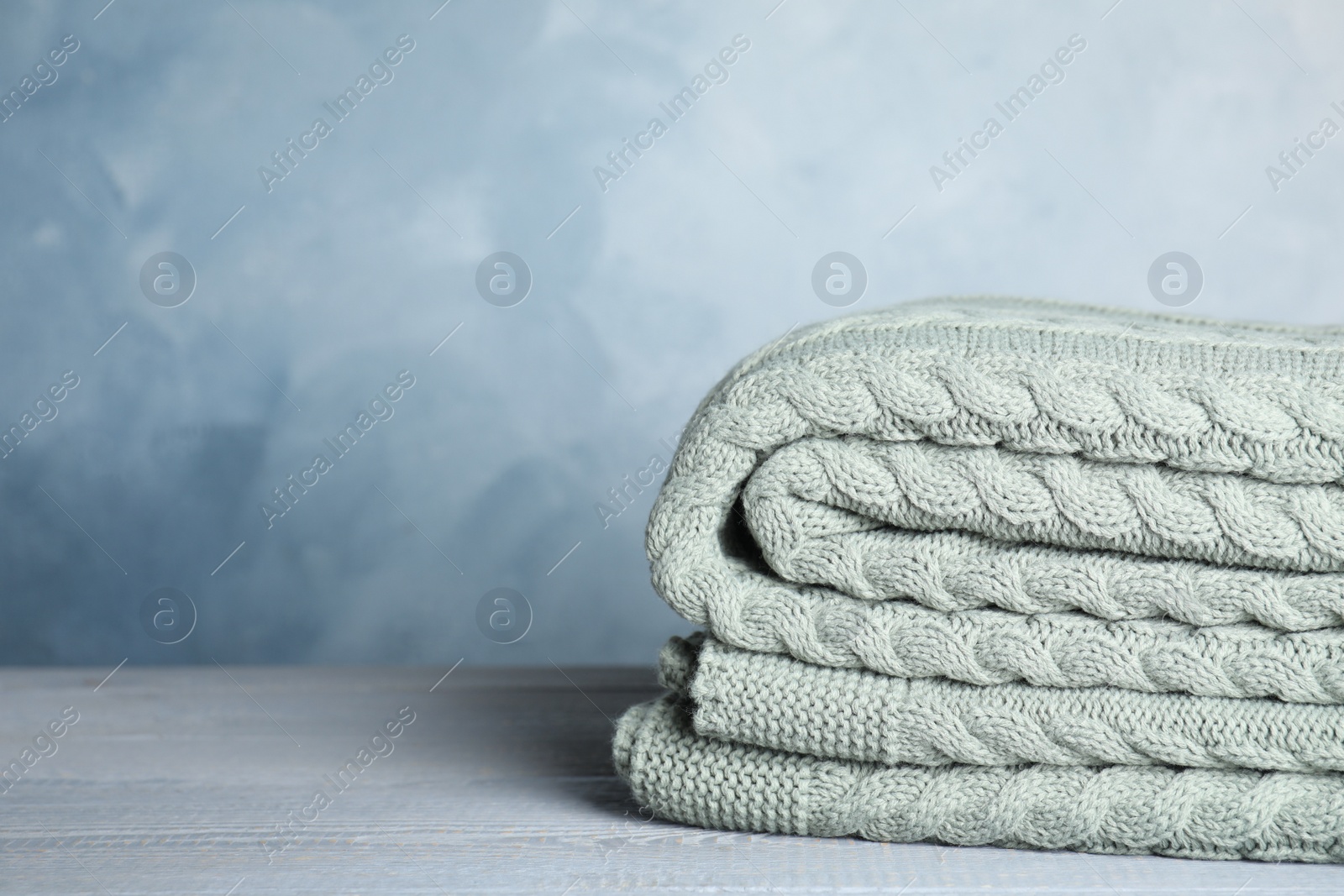 Knitted plaid on light grey wooden table, closeup. Space for text Photo of Knitted plaid on light grey wooden table, closeup. Space for text