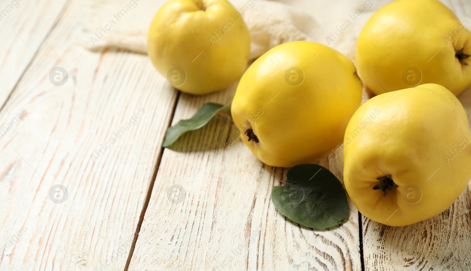 Photo of Fresh ripe organic quinces with leaves on white wooden table. Space for text