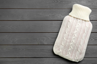 Photo of Hot water bottle with knitted cover on grey wooden background, top view. Space for text