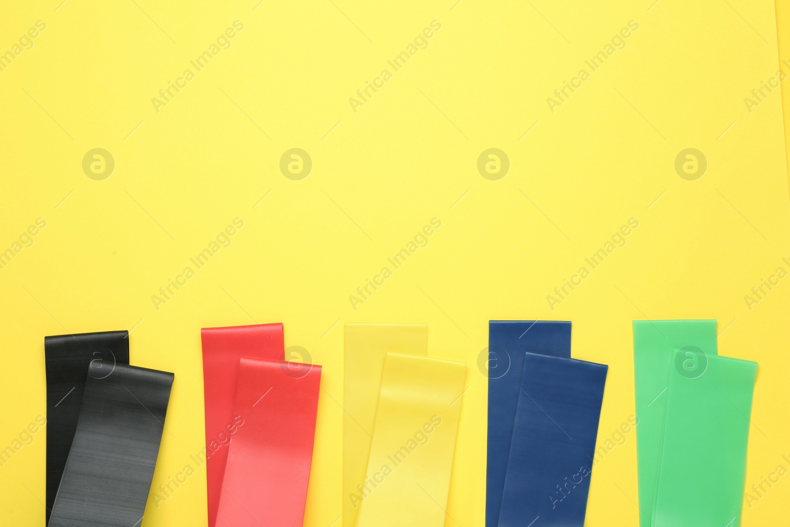Set of fitness elastic bands on yellow background, flat lay. Space for text Photo of Set of fitness elastic bands on yellow background, flat lay. Space for text