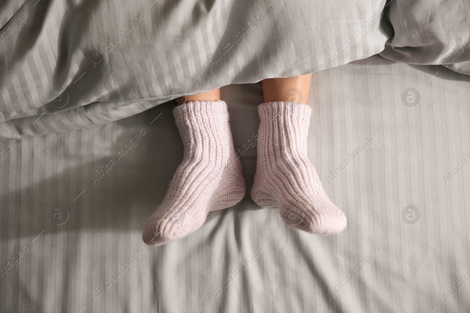 Woman wearing knitted socks under blanket in bed, top view Photo of Woman wearing knitted socks under blanket in bed, top view