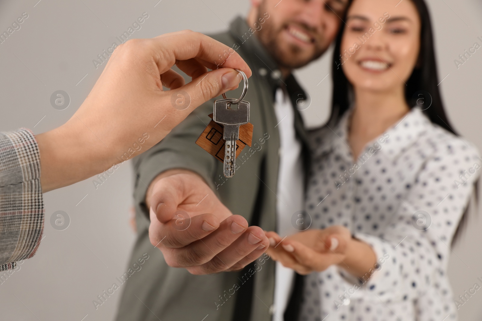 Real estate agent giving key to happy young couple against grey background, closeup Photo of Real estate agent giving key to happy young couple against grey background, closeup