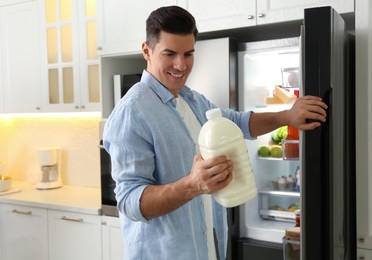 Man with gallon of milk near refrigerator in kitchen Photo of Man with gallon of milk near refrigerator in kitchen