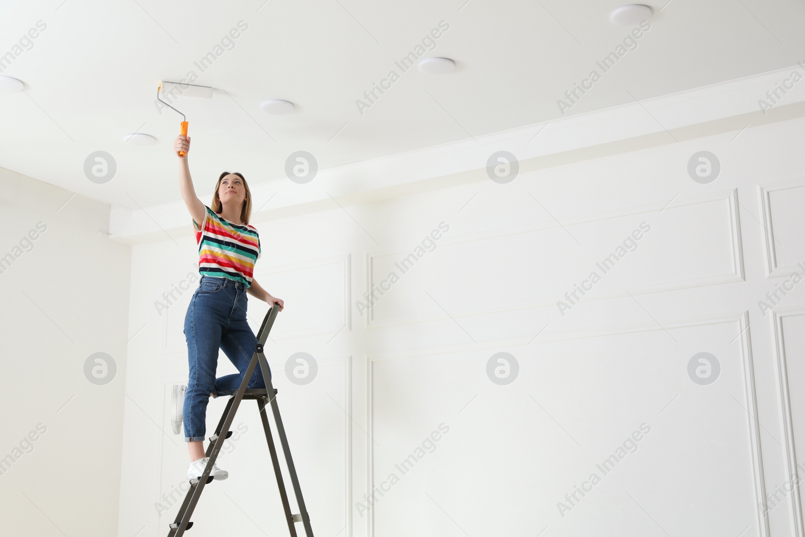 Young woman painting ceiling with white dye indoors, space for text Photo of Young woman painting ceiling with white dye indoors, space for text