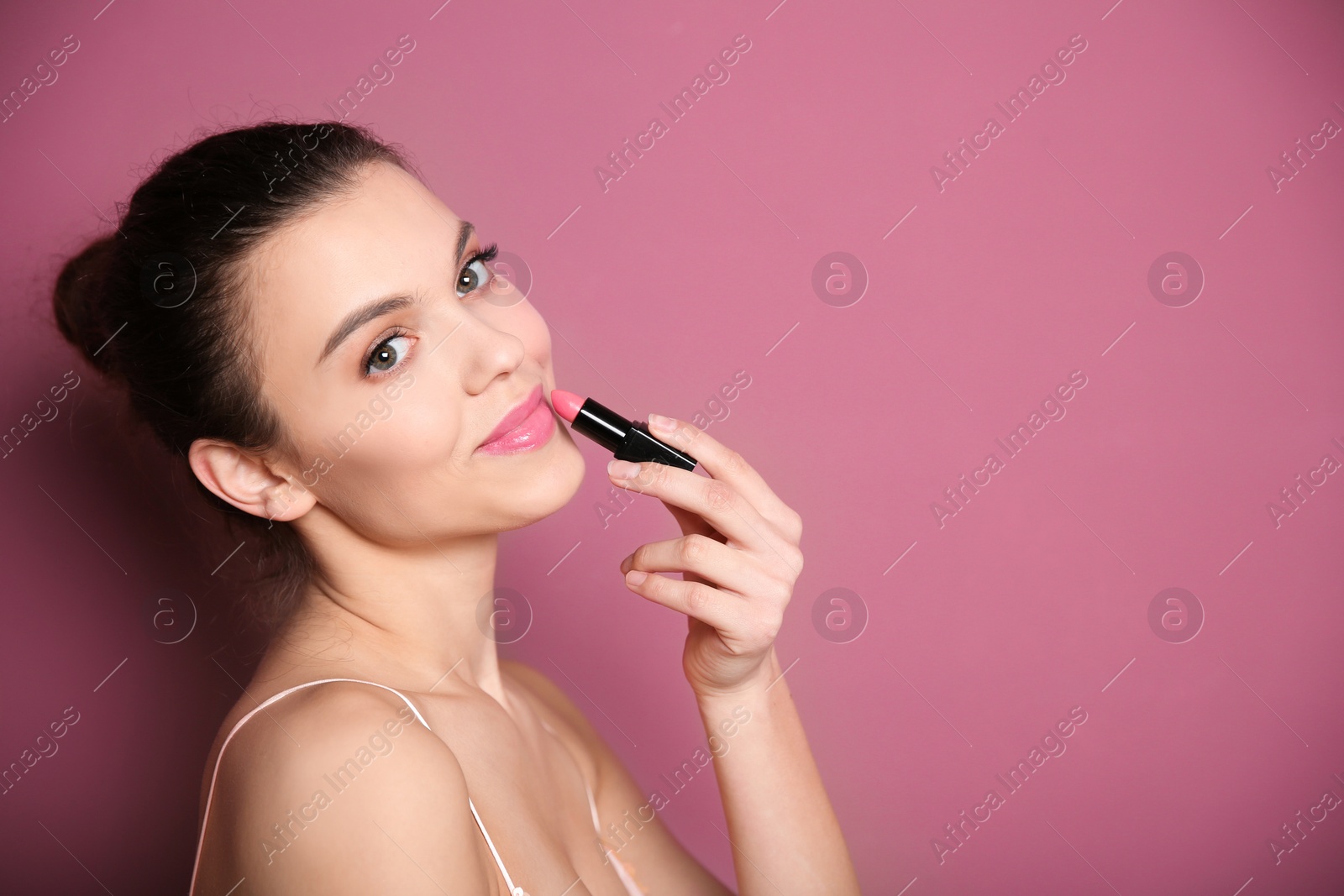 Young woman applying lipstick on color background. Professional makeup products Photo of Young woman applying lipstick on color background. Professional makeup products