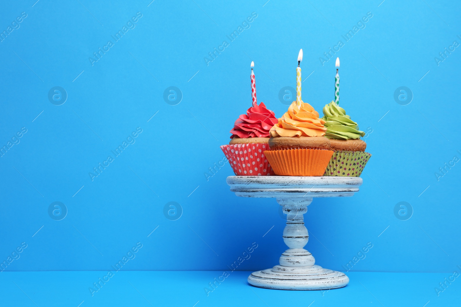 Birthday cupcakes with candles on stand against color background Photo of Birthday cupcakes with candles on stand against color background