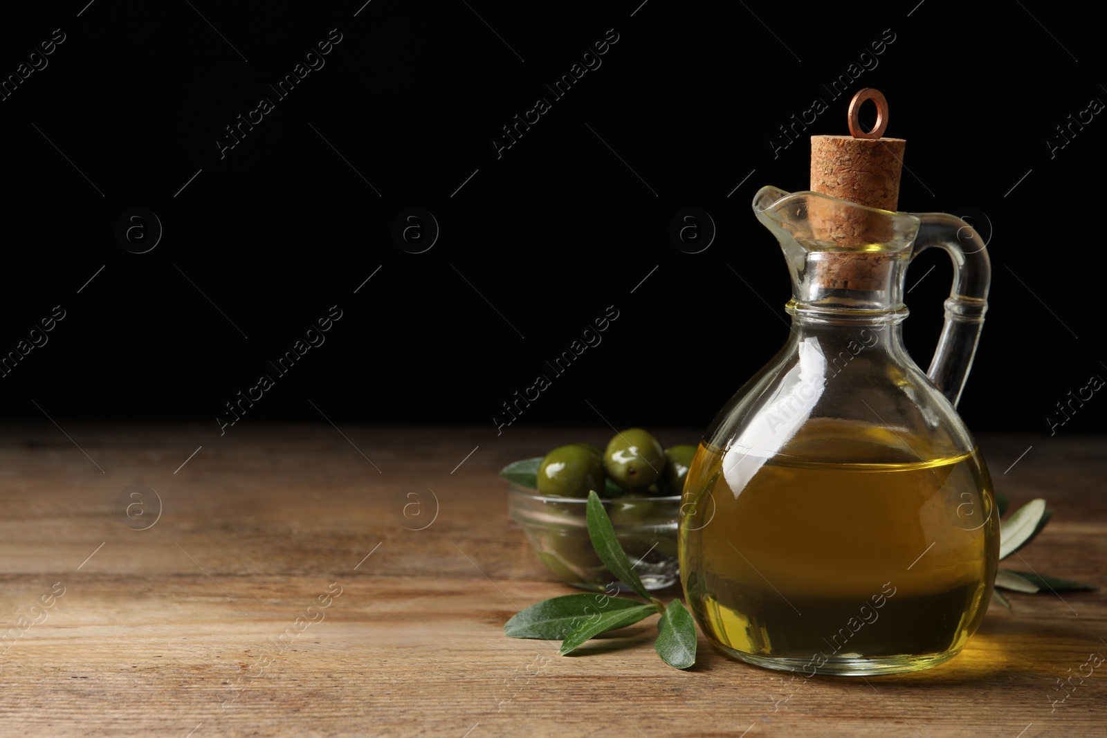 Glass jug of oil, ripe olives and green leaves on wooden table. Space for text Photo of Glass jug of oil, ripe olives and green leaves on wooden table. Space for text
