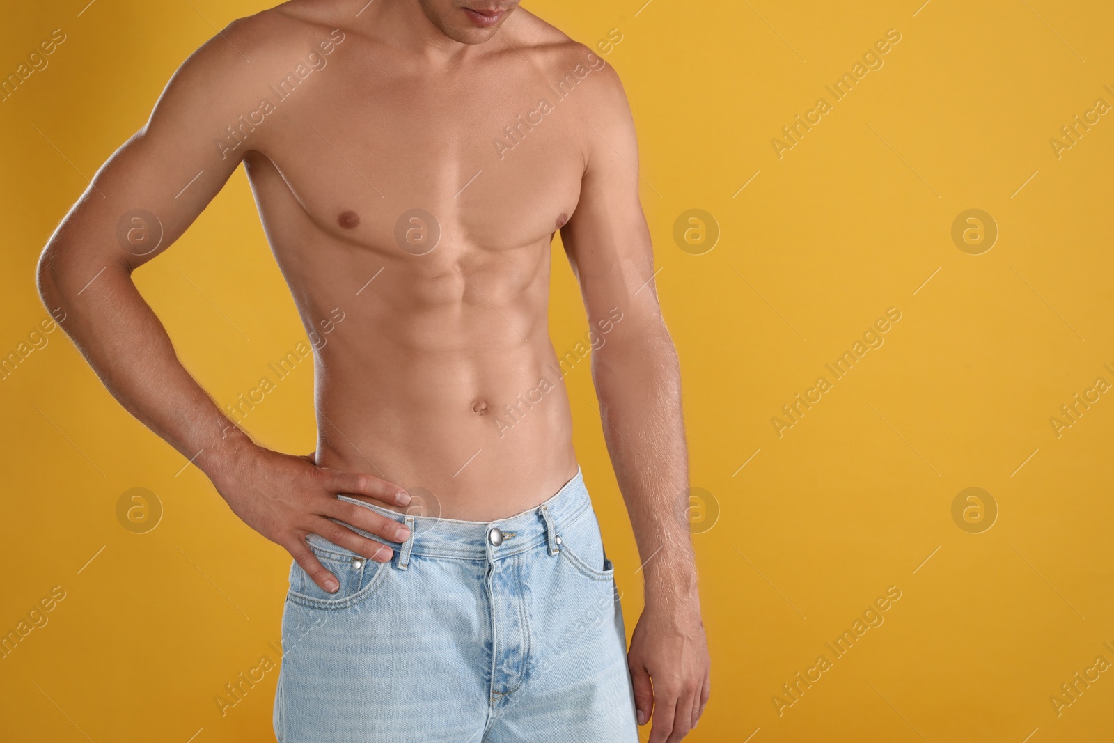 Shirtless man with slim body on yellow background, closeup. Space for text Photo of Shirtless man with slim body on yellow background, closeup. Space for text
