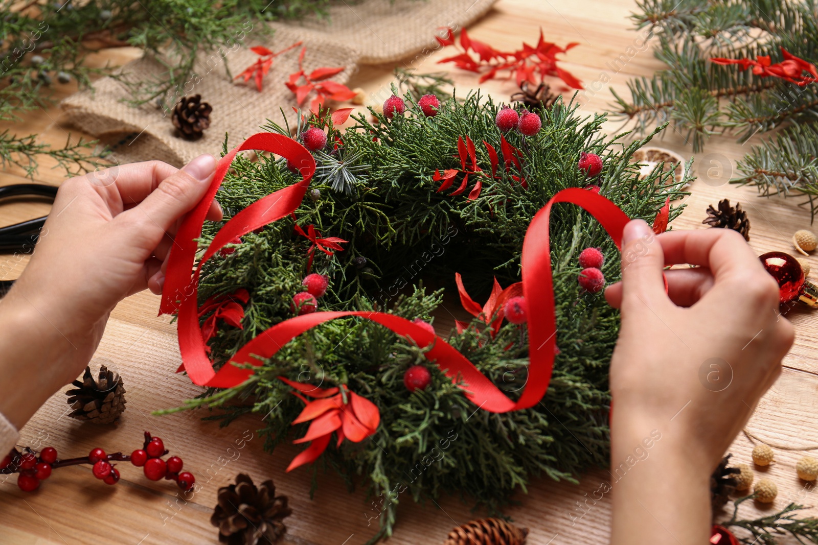 Florist making beautiful Christmas wreath with berries and red ribbon at wooden table, closeup Photo of Florist making beautiful Christmas wreath with berries and red ribbon at wooden table, closeup