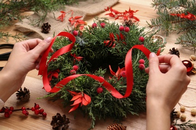 Florist making beautiful Christmas wreath with berries and red ribbon at wooden table, closeup Photo of Florist making beautiful Christmas wreath with berries and red ribbon at wooden table, closeup