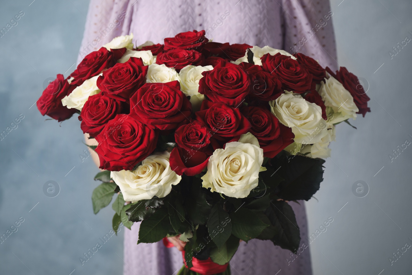 Woman holding luxury bouquet of fresh roses on light blue background, closeup Photo of Woman holding luxury bouquet of fresh roses on light blue background, closeup