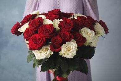 Woman holding luxury bouquet of fresh roses on light blue background, closeup Photo of Woman holding luxury bouquet of fresh roses on light blue background, closeup
