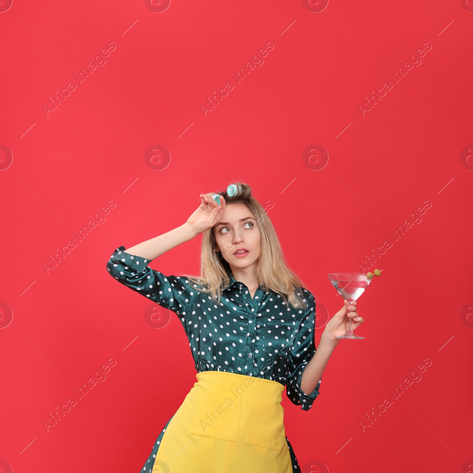 Young housewife with glass of martini on red background Photo of Young housewife with glass of martini on red background