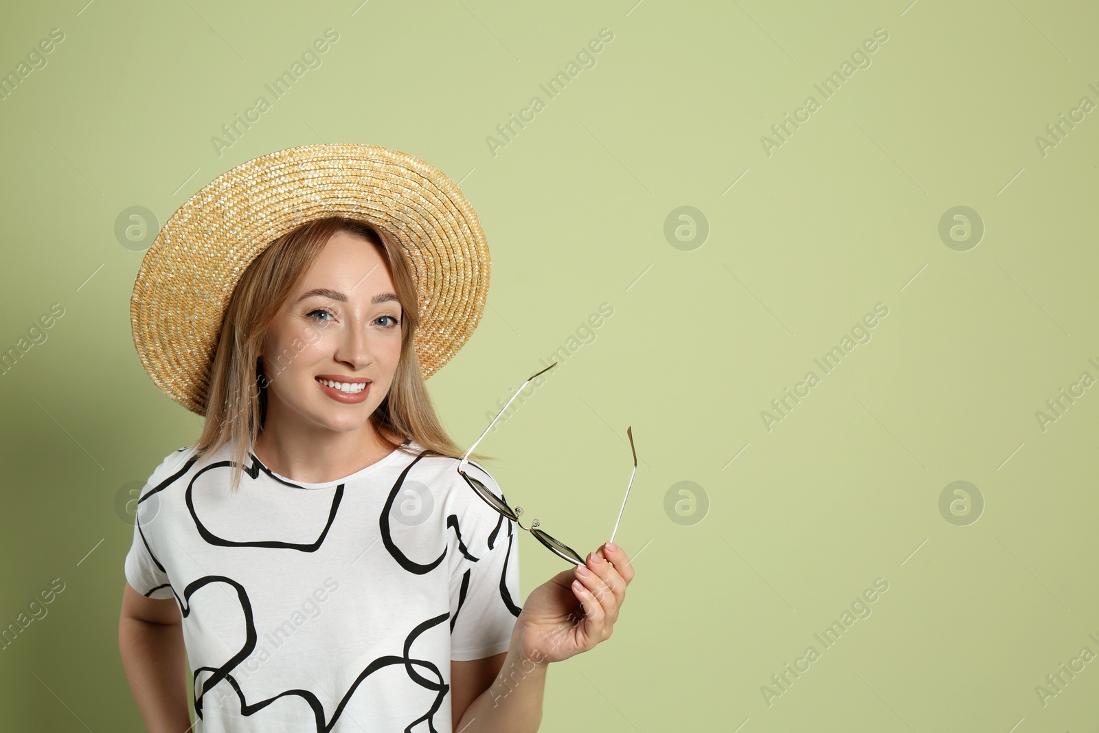 Photo of Beautiful young woman with straw hat and sunglasses on light green background, space for text. Stylish headdress
