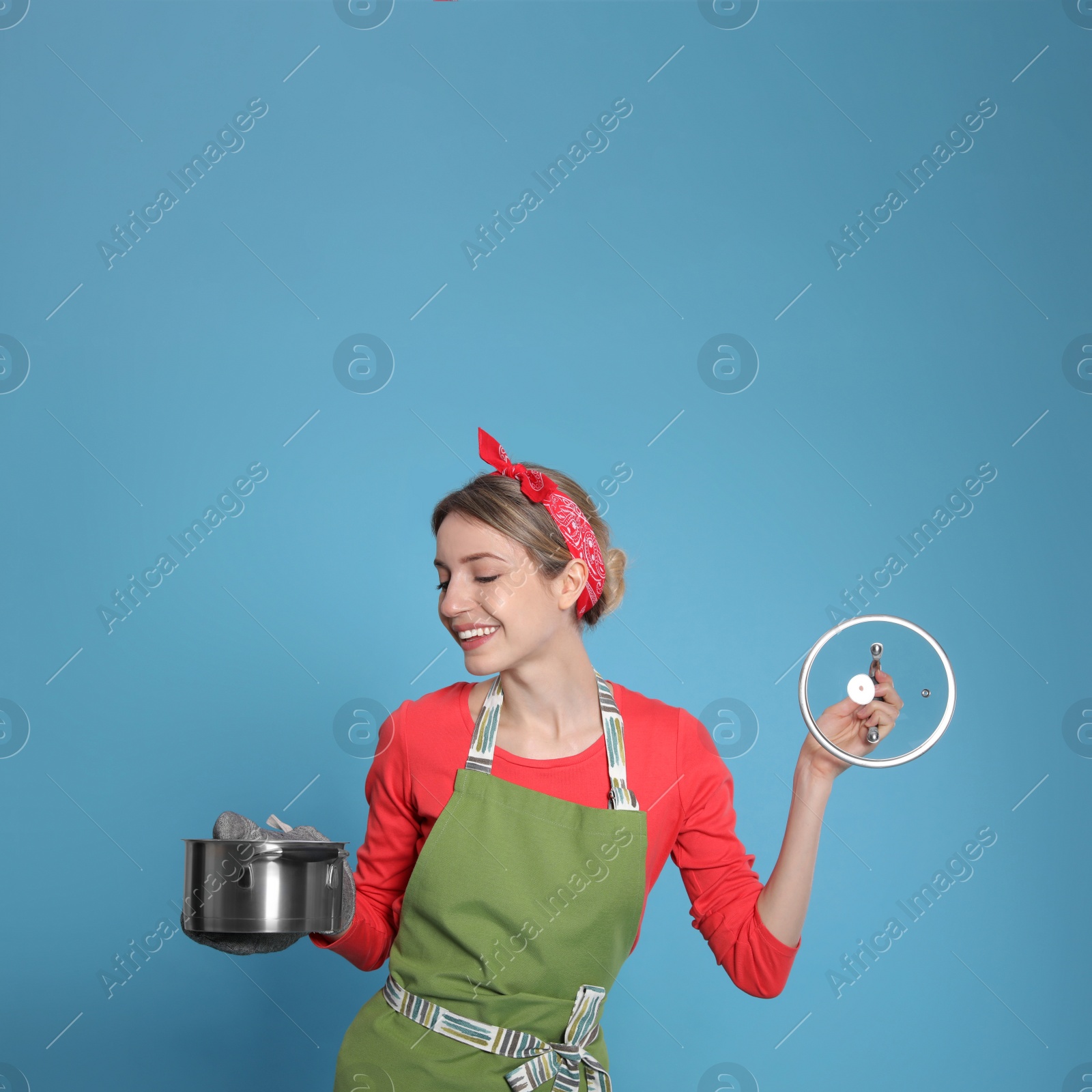 Young housewife with pot on light blue background Photo of Young housewife with pot on light blue background