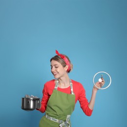 Young housewife with pot on light blue background Photo of Young housewife with pot on light blue background