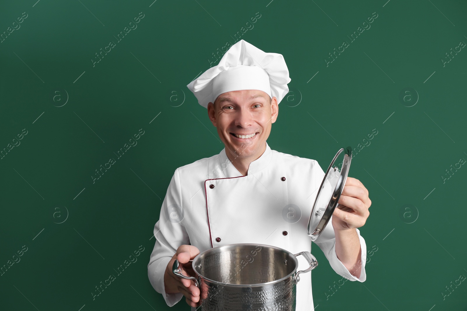 Happy male chef with cooking pot on dark green background Photo of Happy male chef with cooking pot on dark green background