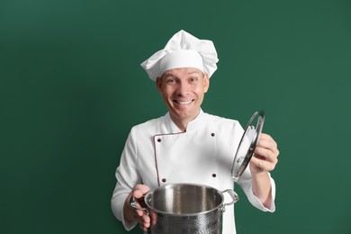 Happy male chef with cooking pot on dark green background Photo of Happy male chef with cooking pot on dark green background